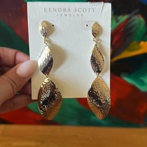 Kendra Scott long gold earrings in a hammered metal finish.